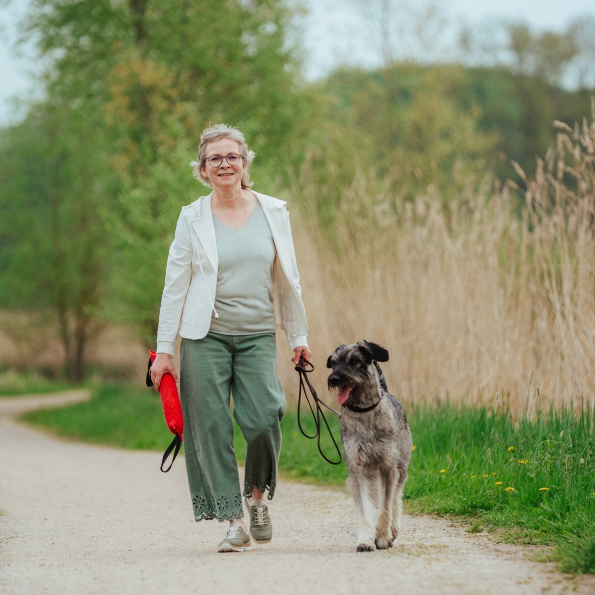 Dorothea Brandes mit Therapiehündin Martha Dorothea trägt ein Spielzeug in der Hand und macht einen Spaziergang mit ihrer Hündin Martha